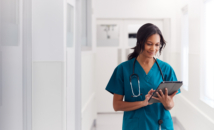 Female Doctor Wearing Scrubs In Hospital Corridor Using Digital Tablet